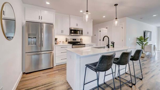 A modern kitchen with white cabinetry, stainless steel appliances, and a central island with bar stools.
