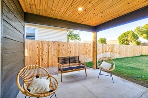 Eine überdachte Terrasse mit zwei Korbstühlen und einer Holzbank.