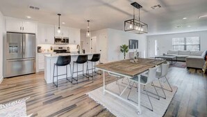A modern kitchen with white cabinets, stainless steel appliances, a wooden dining table, and a bar area.