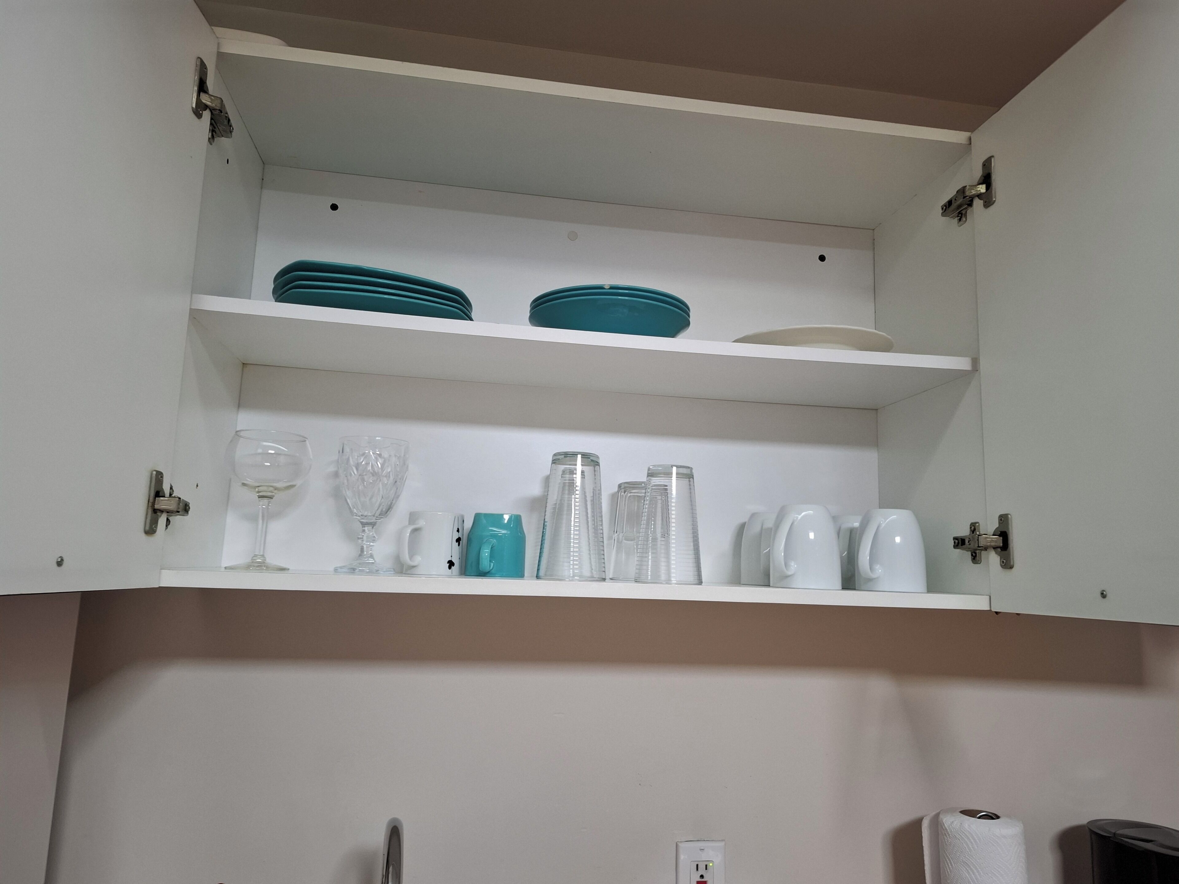 Un mueble de cocina con estantes que contienen vajilla, vasos y una cafetera.