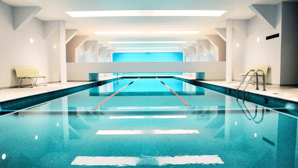 Un'ampia piscina coperta con corsie ben delimitate, una panchina per lato e un design architettonico moderno.