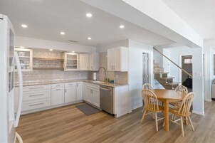 Una cocina moderna con armarios blancos, encimera de granito y zona de comedor con sillas de madera.