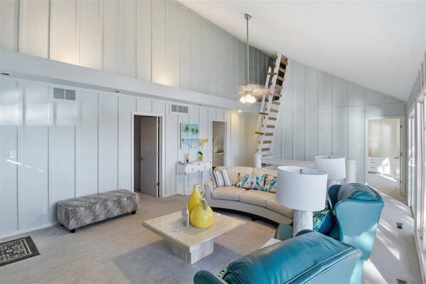 A spacious living room with a high ceiling, a built-in bench, a curved sofa, and a staircase.