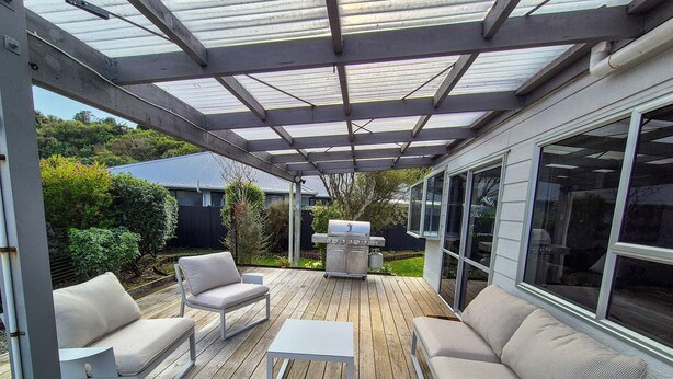 A covered patio with wooden flooring, white furniture, and a grill. - Comfy family home, stay at our retreat on Brittan St! (Hokitika)