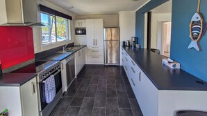 A modern kitchen with stainless steel appliances, a red refrigerator, and a blue accent wall. - Comfy family home, stay at our retreat on Brittan St! (Hokitika)