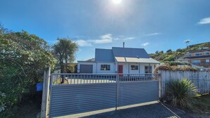 A residential property with a gated entrance, a garage, and a house with a red door. - Comfy family home, stay at our retreat on Brittan St! (Hokitika)