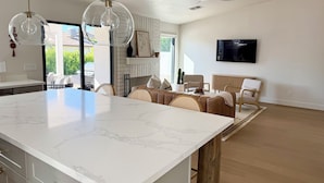 A modern kitchen with a marble island, pendant lights, and a dining area with wicker furniture. - Peaceful 3BD/2BA Dog-Friendly Paradise Posada (Scottsdale)