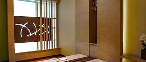 A traditional Japanese room with tatami flooring, a low table with a placemat, and a sliding door with a geometric pattern.