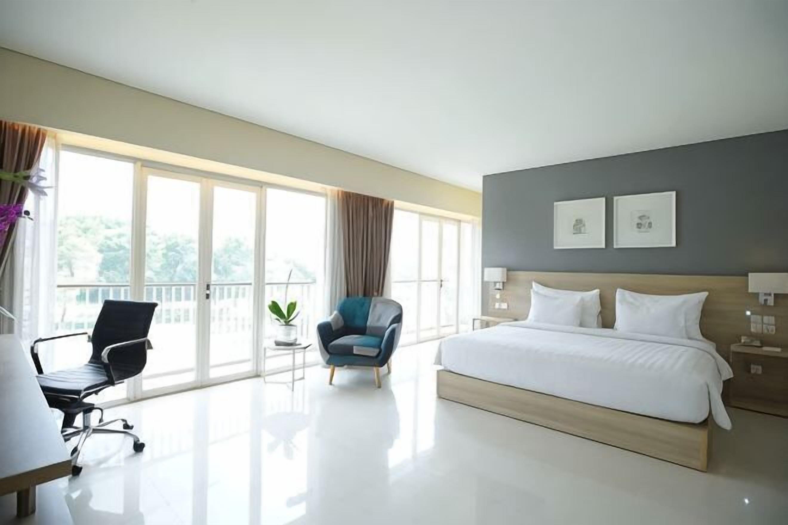 Une chambre d’hôtel avec un grand lit, un bureau, une chaise, une petite table et un balcon avec vue.