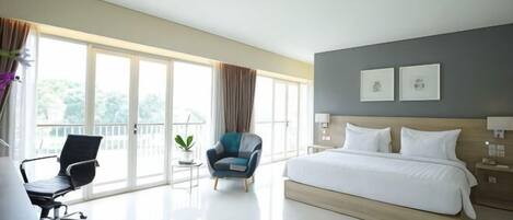 A hotel room with a large bed, a desk, a chair, a small table, and a balcony view.