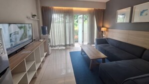 A modern living room with a flat-screen TV, a sofa, a coffee table, and a balcony with curtains. - TreePark Karawang (East Telukjambe)