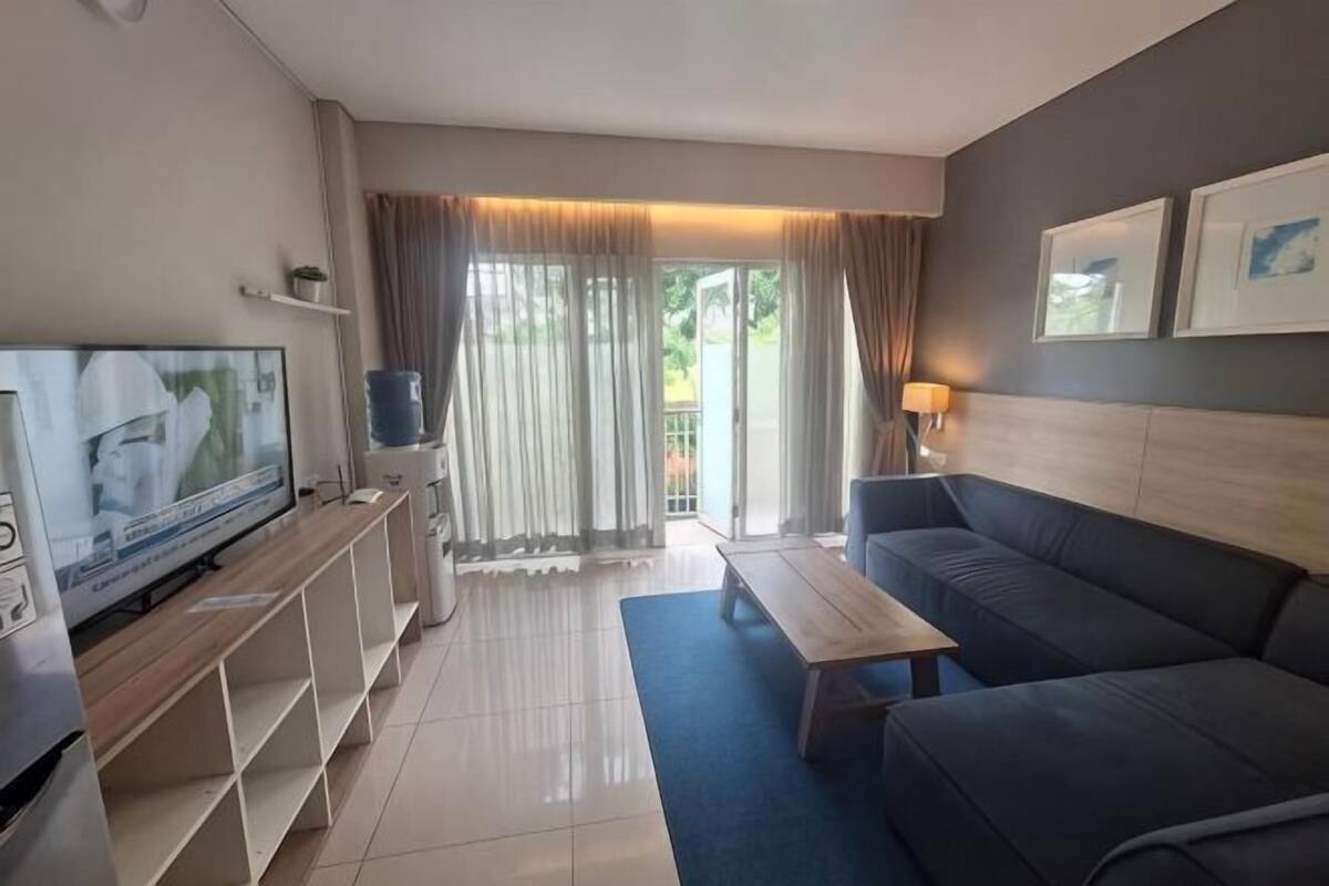 Un salón moderno con una televisión de pantalla plana, un sofá, una mesa de centro y un balcón con cortinas.