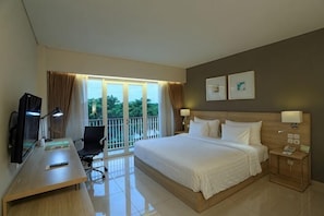 A hotel room with a bed, desk, chair, TV, and a balcony with curtains. - TreePark Karawang (East Telukjambe)