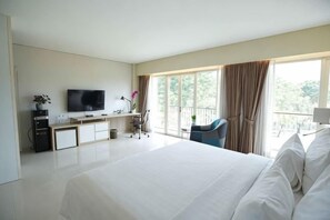A hotel room with a large bed, a desk with a computer, a television, and a balcony with a chair. - TreePark Karawang (East Telukjambe)