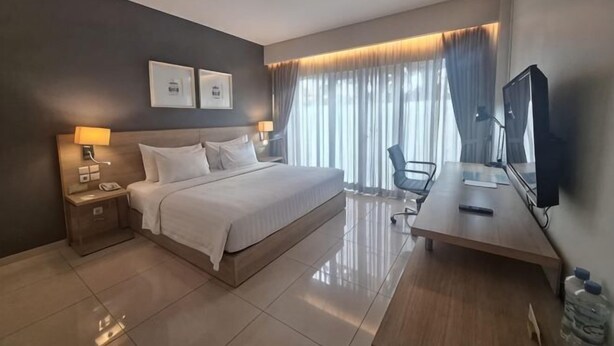 A hotel room with a bed, bedside tables, a desk, a chair, a television, and curtains. - TreePark Karawang (East Telukjambe)