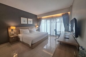 Habitación de hotel con cama, mesitas de noche, escritorio, silla, televisor y cortinas.