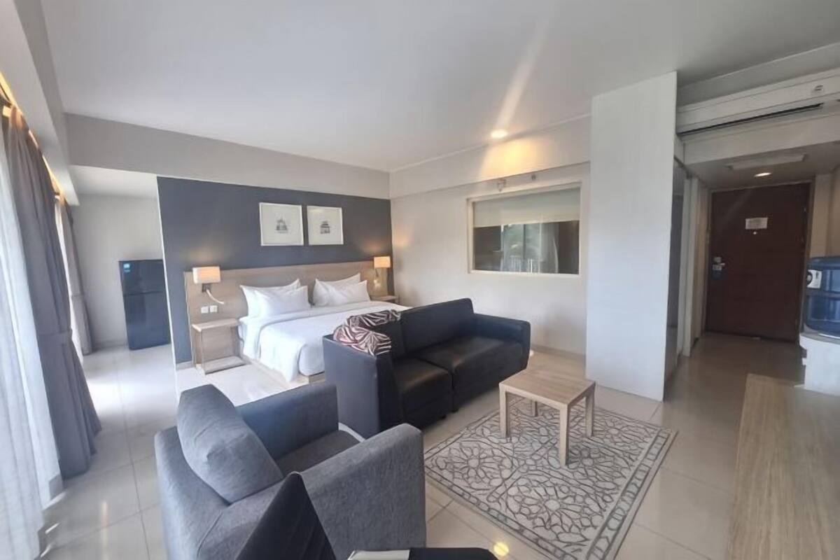 Una habitación de hotel moderna con una cama, dos sofás, una mesa de centro y un ventanal grande.