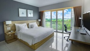 A hotel room with a large bed, a desk with a computer, a chair, a nightstand, and a view of the outdoors. - TreePark Karawang (East Telukjambe)