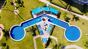 An aerial view of a hotel with a large central pool, multiple lounge areas, and surrounding greenery.