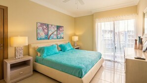 A bedroom with a bed, two bedside tables, a ceiling fan, and a window with a view of buildings.