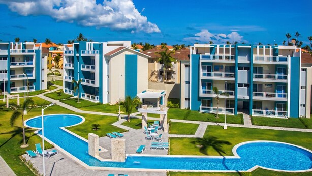 A resort with multiple blue and white buildings, a central swimming pool, and a well-maintained lawn.