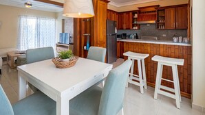 A modern kitchen with wooden cabinets, a central island, and a dining area with a white table and chairs.