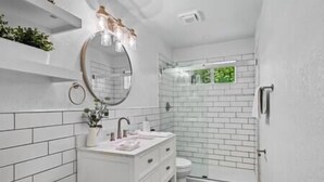 Een moderne badkamer met witte tegels, een glazen douchecabine en een wastafelmeubel met spiegel en verlichting.