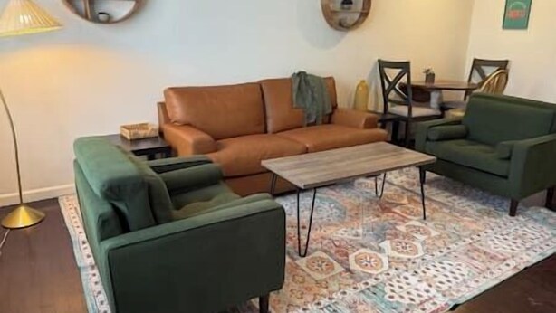Een woonkamer met een bruine leren bank, een groene fauteuil, een houten salontafel en een kamerbreed tapijt met een patroon.