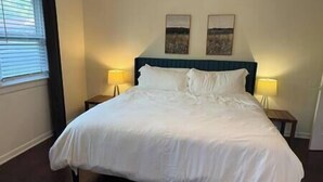 Een net opgemaakt bed met witte lakens in een hotelkamer. Daarboven hangen twee schilderijen aan de muur.