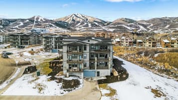 A multi-story residential building with a modern architectural design, surrounded by a snowy landscape and mountains in the background.