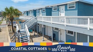 Una cabaña costera con balcón, una escalera y un letrero que dice Coastal Cottages by Beach Box.