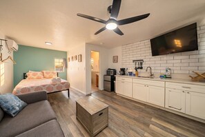Un espace de vie compact comprenant un lit, un canapé, une kitchenette et un ventilateur de plafond.