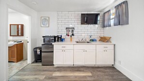 Una cocina moderna con armarios blancos, un microondas, una cafetera y un televisor montado sobre la encimera.