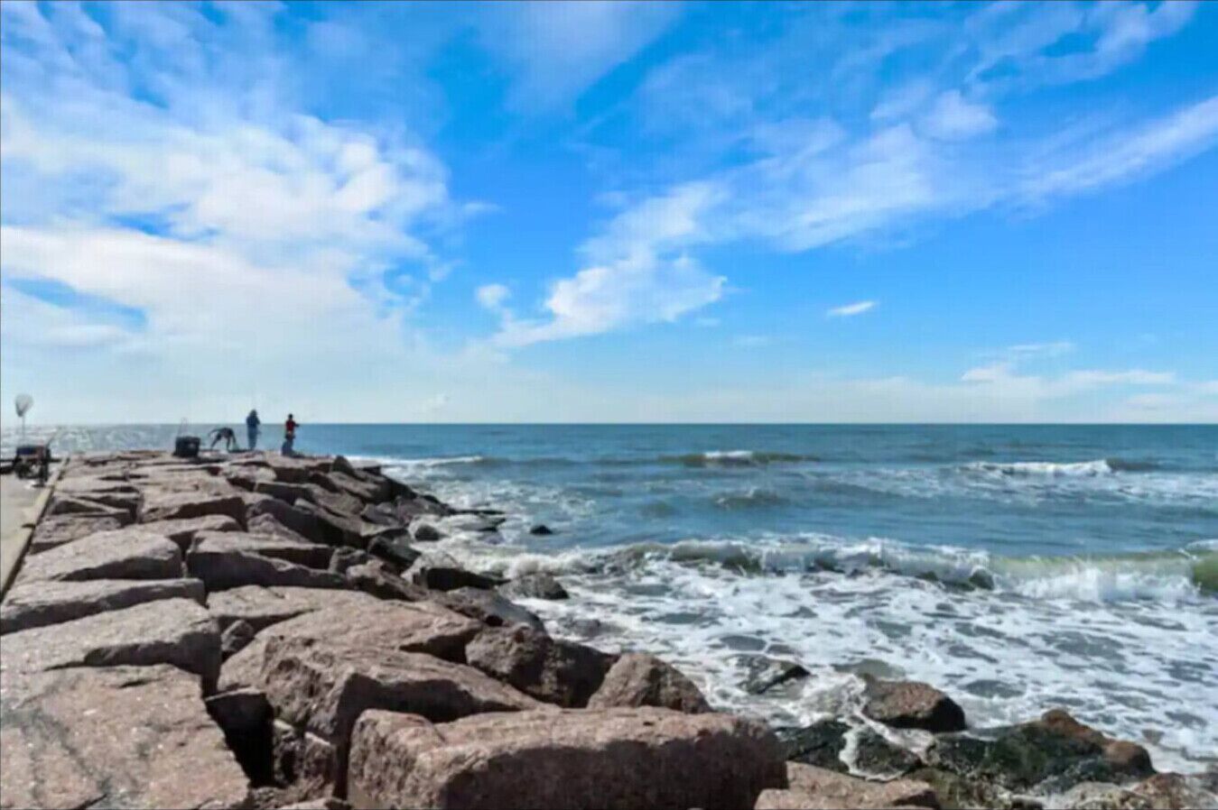 Une jetée rocheuse qui s’avance dans la mer, les vagues s’y brisant.
