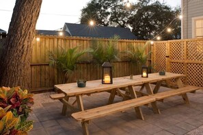 A wooden picnic table with benches and lanterns, surrounded by a wooden fence and potted plants. - Charming Historic Home by Beach & Strand (Galveston)