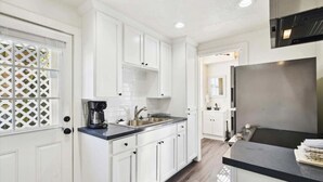 A modern kitchen with white cabinets, a black countertop, and a stainless steel refrigerator. - Charming Historic Home by Beach & Strand (Galveston)