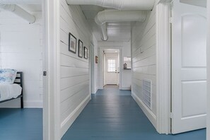 A narrow hallway with white walls and blue flooring, leading to a door at the end. - Charming Historic Home by Beach & Strand (Galveston)
