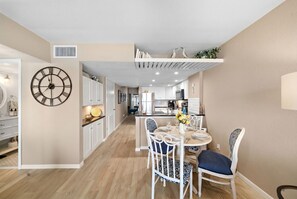 Una cocina moderna con armarios blancos, un comedor con una mesa redonda y sillas, y un gran reloj de pared.