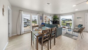 A spacious living area with a dining table, sofas, and a balcony with a view. - Charming Beach House Near Water & Fishing (Surfside)