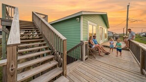 A wooden deck with a staircase leading to a small green building, possibly a guest house or storage shed. - Charming Beach House Near Water & Fishing (Surfside)