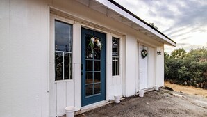 Een wit gebouw met een blauwe deur, twee ramen en een klein portaal met witte plantenbakken.