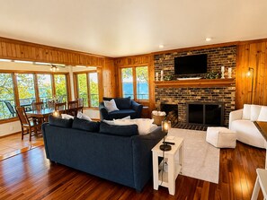 A spacious living area with a fireplace, wooden walls, a television, and a dining area with a view.