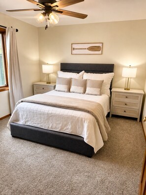 A bedroom with a bed, two bedside tables, a ceiling fan, and a window with curtains.