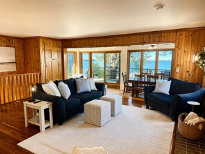 A cozy living room with wooden walls, a dark blue sofa set, a white coffee table, and a dining area with a wooden table and chairs.