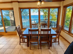 A dining area with a table and chairs, large windows with a view of the sea, and a ceiling fan.