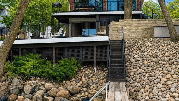 Ein modernes Haus mit Terrasse, das auf ein Gewässer mit Blick von Bäumen aus blickt.