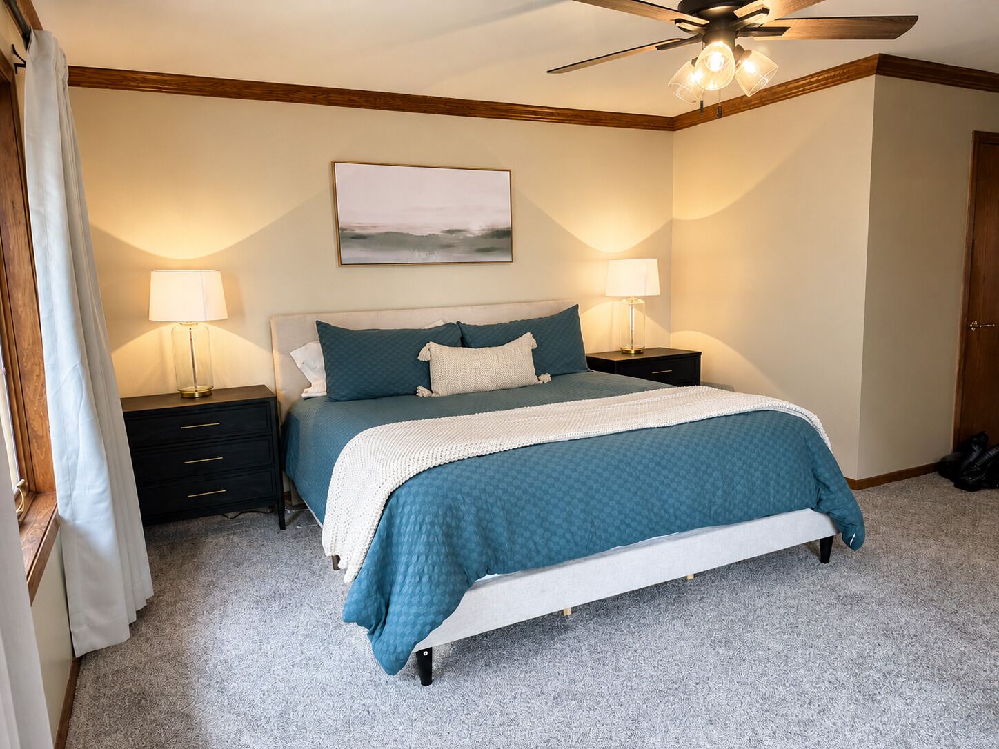 A bedroom with a bed, two bedside tables, a ceiling fan, and a painting on the wall.