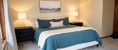 A bedroom with a bed, two bedside tables, a ceiling fan, and a painting on the wall.