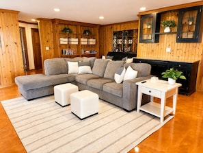 Ein Wohnzimmer mit Ecksofa, Hocker, einem weißen Beistelltisch und einem Kamin.