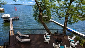 Eine Holzterrasse mit Liegestühlen und einem Feuerkorb, mit Blick auf einen See mit Booten und einem Steg.